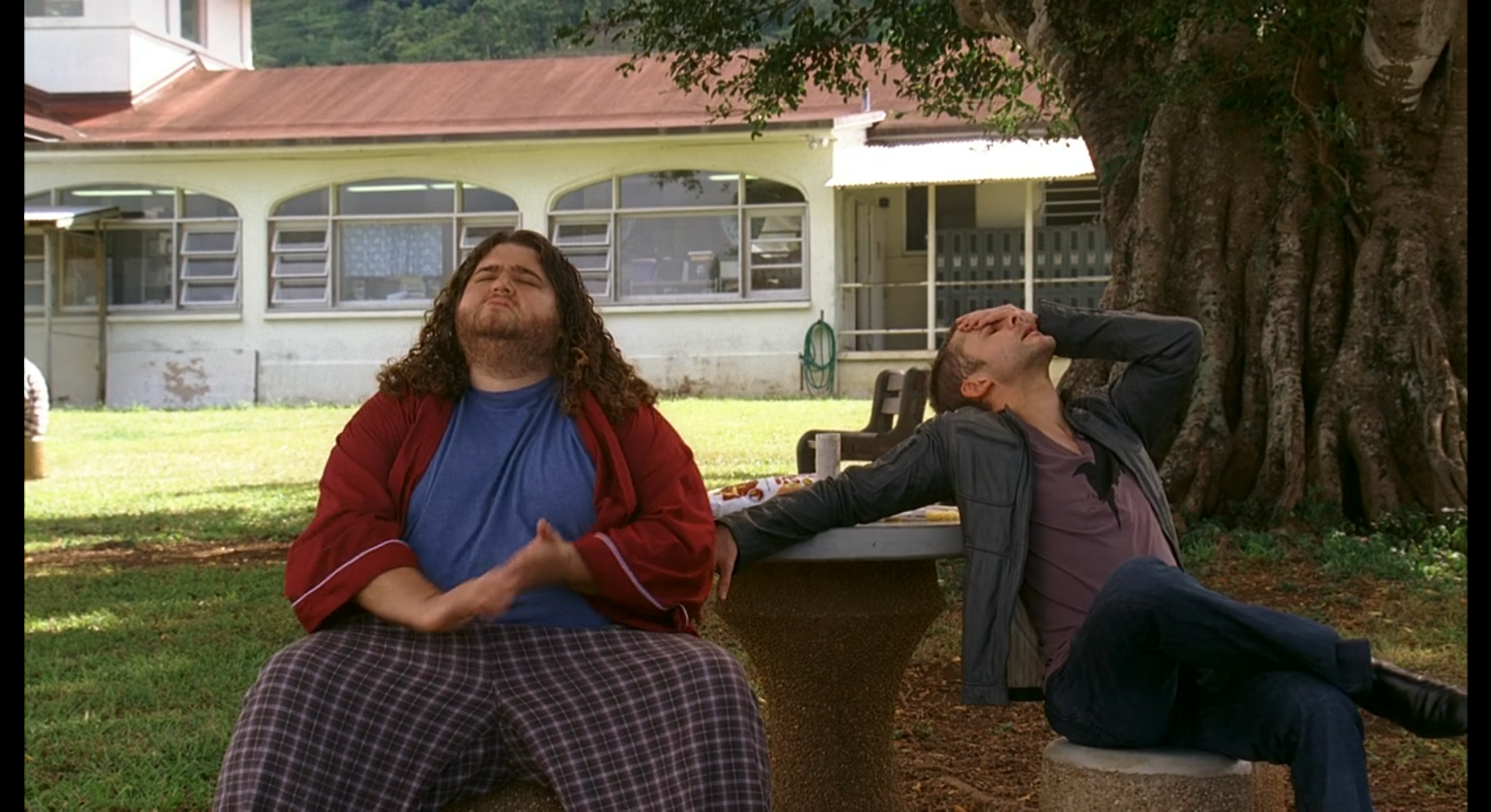 Hurley and Charlie sit at an outdoor table under a tree.